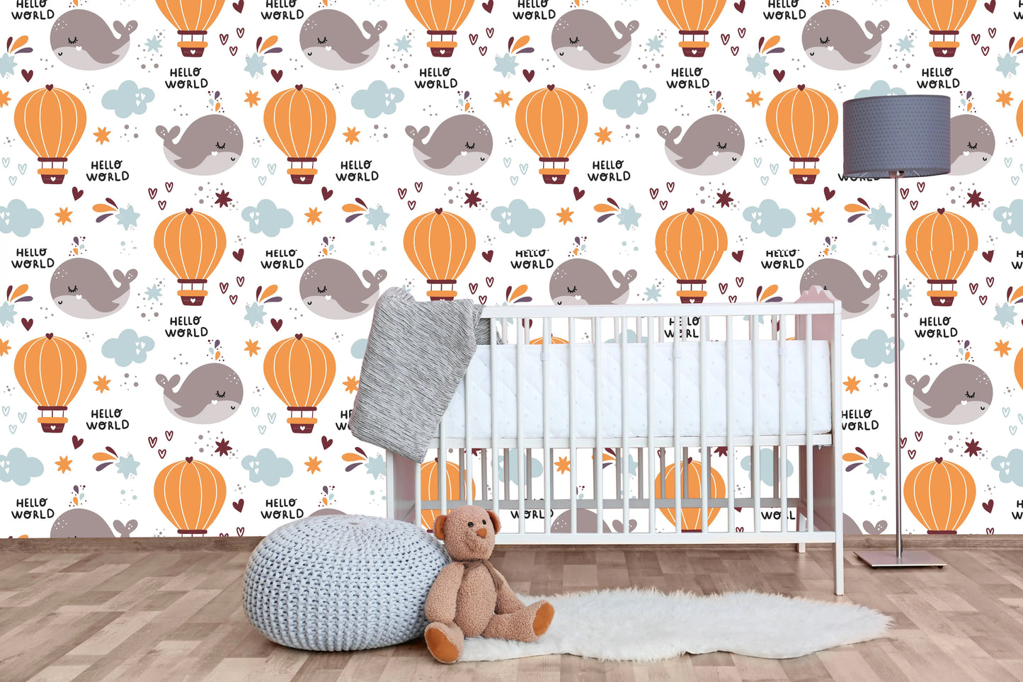 Hello World whale nursery wallpaper behind a white crib with a knit pouf and teddy bear