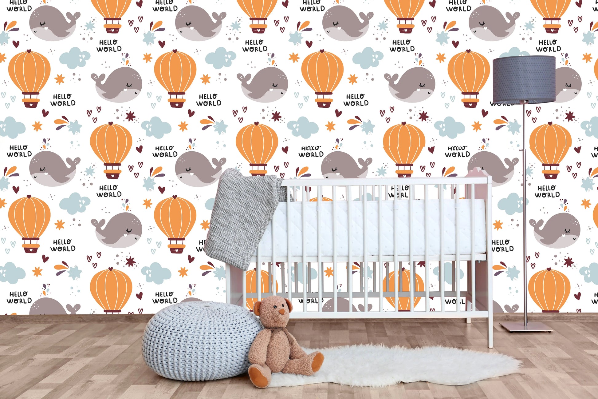 Hello World whale nursery wallpaper behind a white crib with a knit pouf and teddy bear